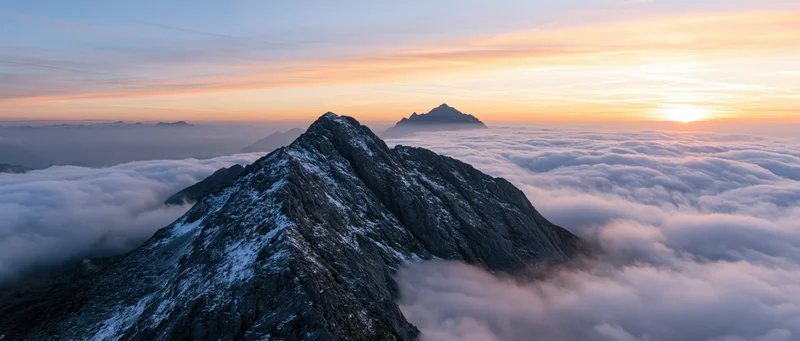 Snow-covered mountain peak rising above a sea of clouds at sunrise