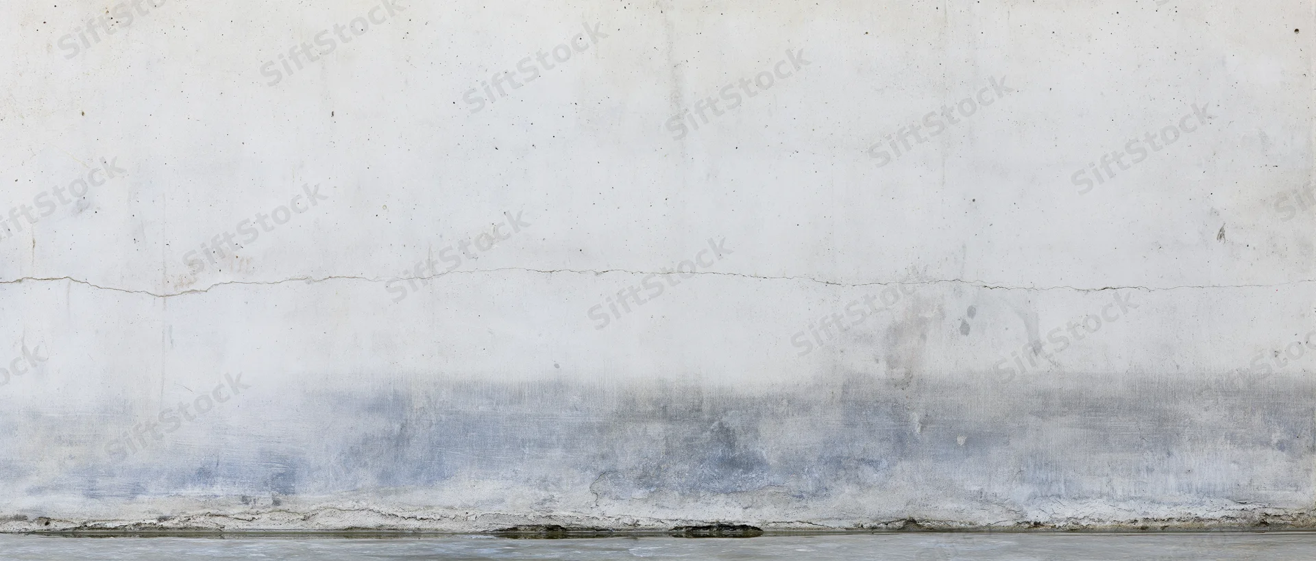 Weathered concrete wall with horizontal crack and damp stain near base