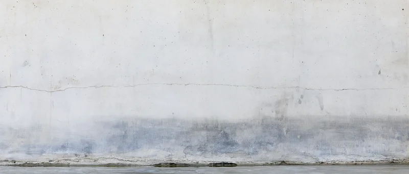 Weathered concrete wall with horizontal crack and damp stain near base