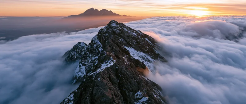 Snow-dusted mountain peak rising above a sea of clouds at sunrise