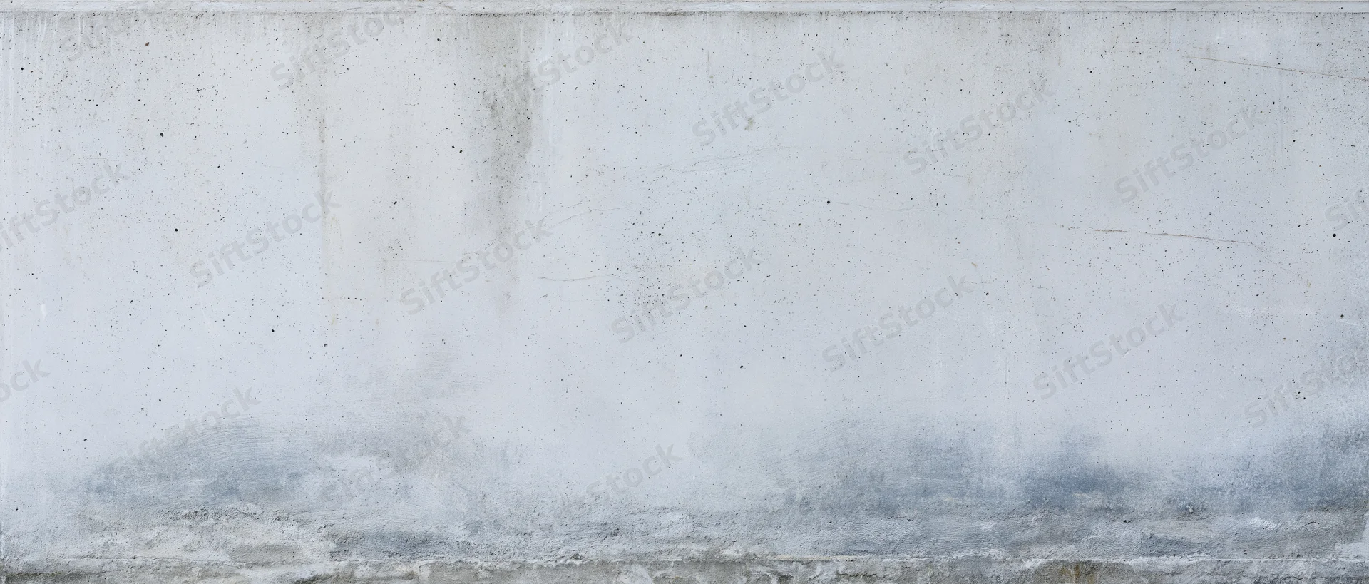 Weathered concrete wall with gray stains and speckles, showing rough texture and horizontal seam, used as a backdrop