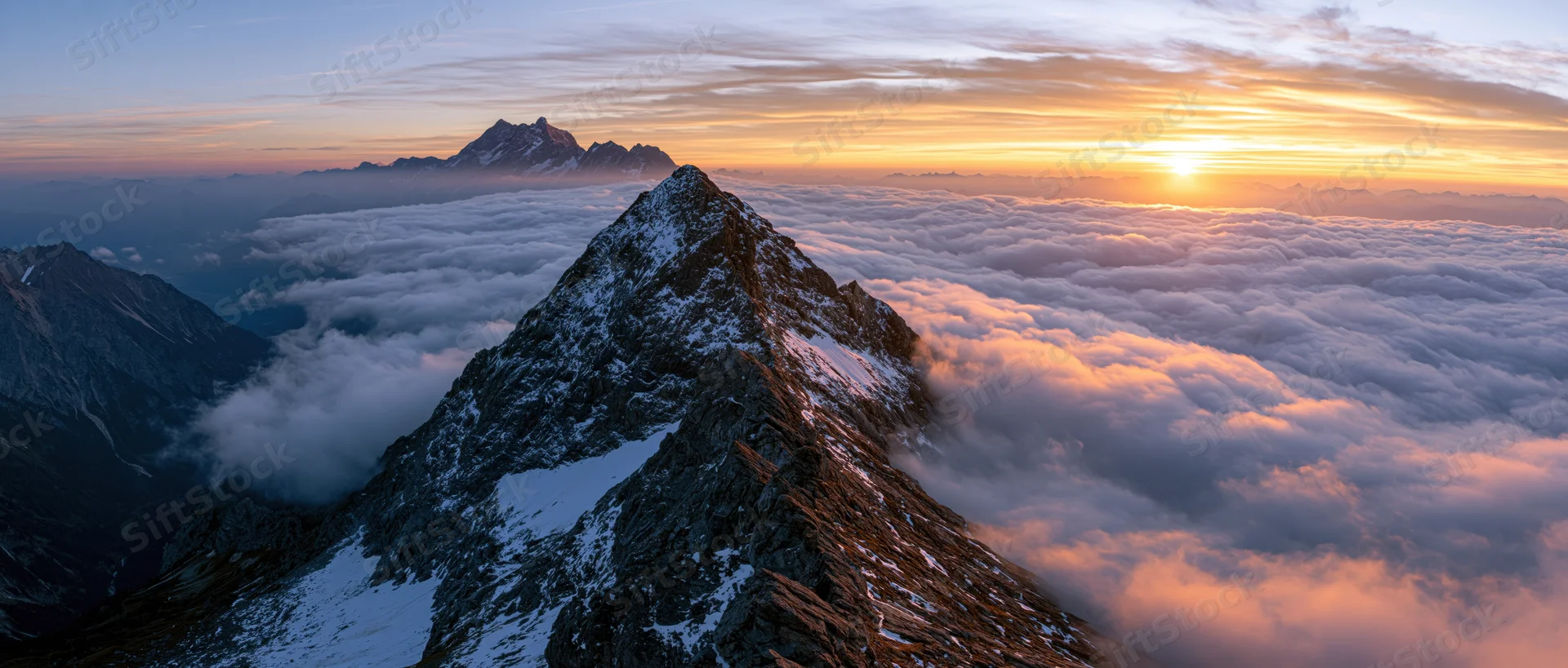 Snow-covered mountain peak rising above a sea of clouds at sunrise