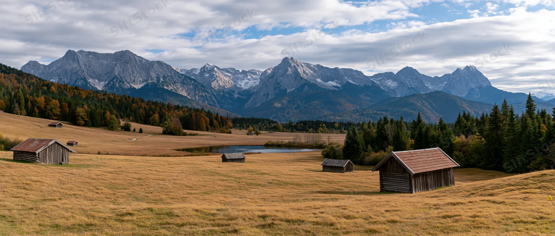 Alpine meadow with wooden cabins and snow-capped mountains in autumn