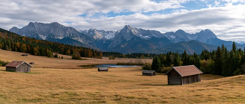 Alpine meadow with wooden cabins and snow-capped mountains in autumn