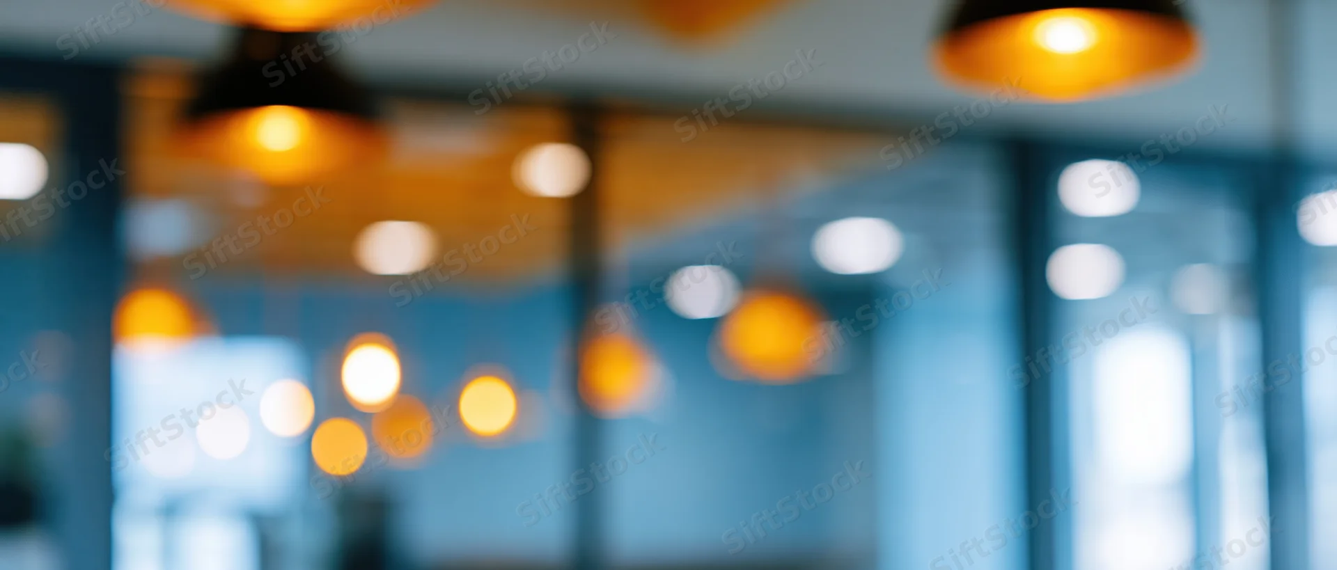 Blurred interior view of an office space with warm pendant lights and glass partitions creating a modern workspace ambiance