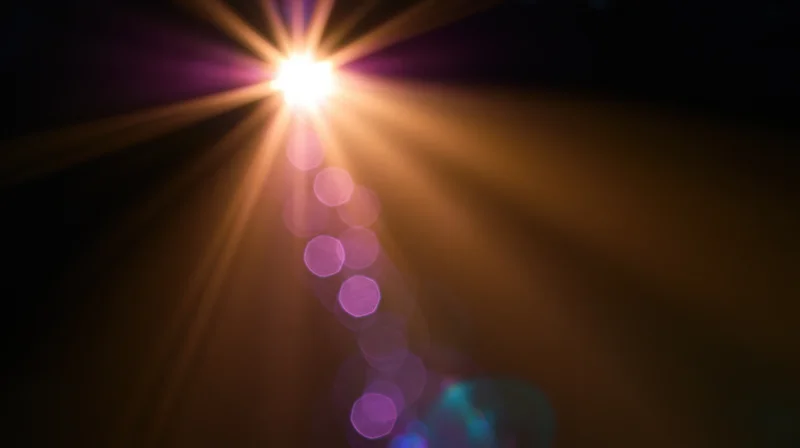 Bright light source emitting starburst rays and purple bokeh circles against dark background