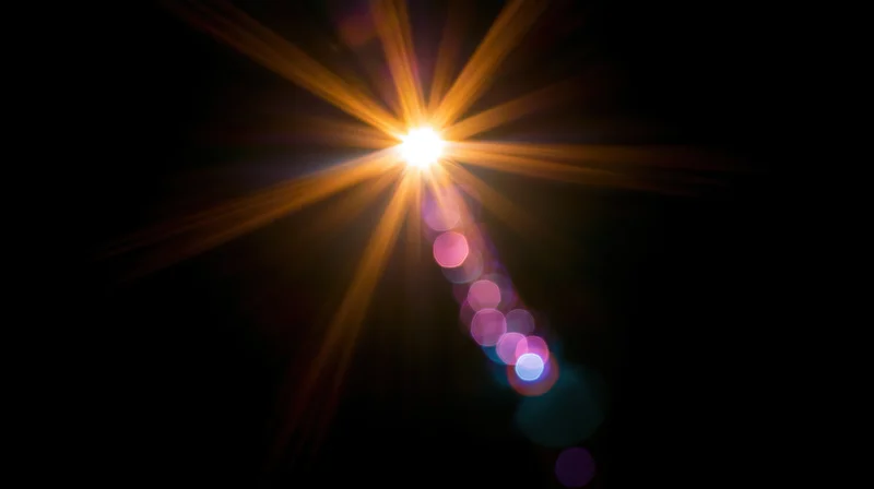 Bright starburst light with colorful bokeh trails on dark background