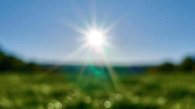 Bright sun shining over a green grassy field under a clear blue sky
