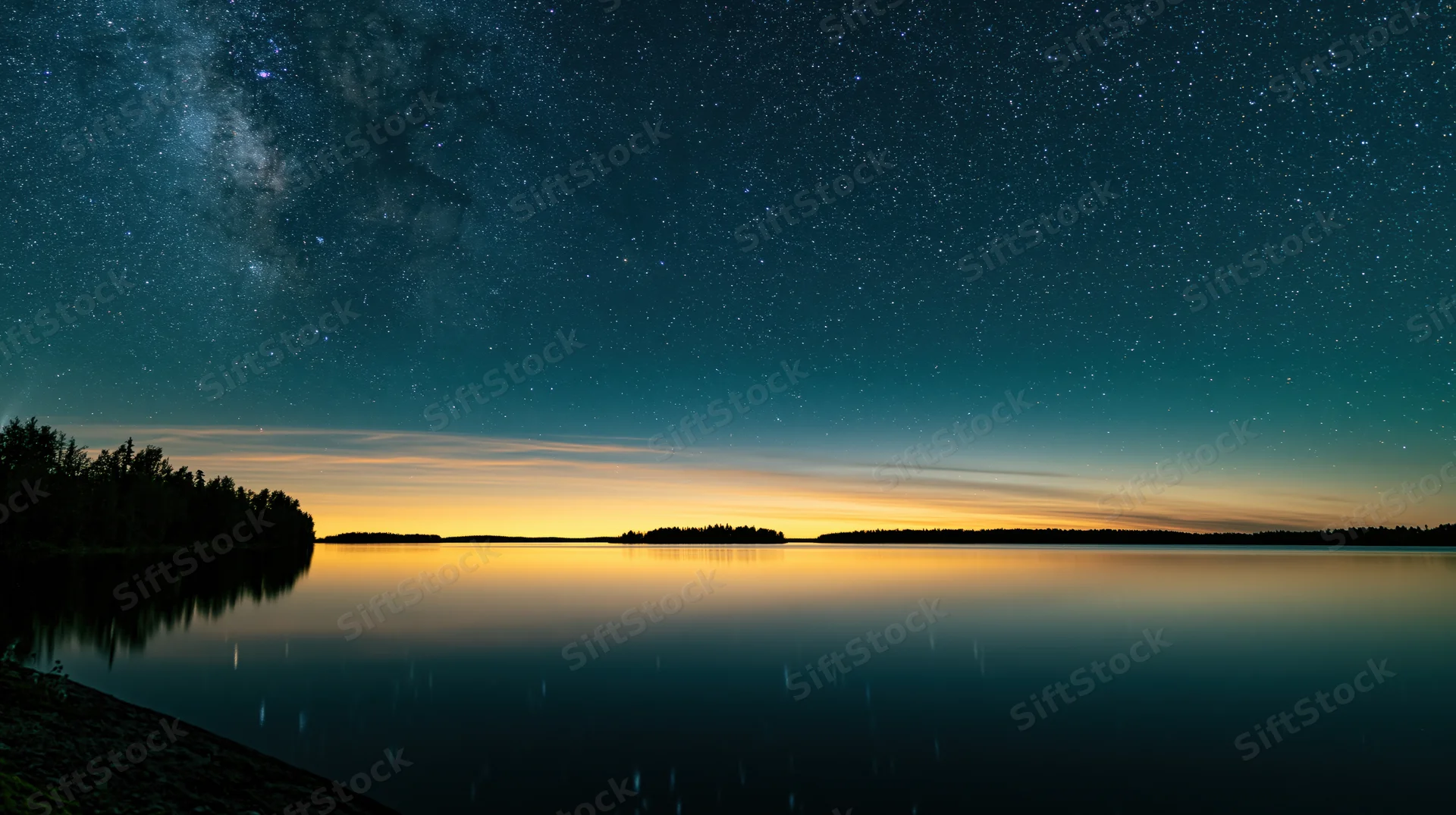 Milky way reflected in calm lake waters at twilight with forested shoreline