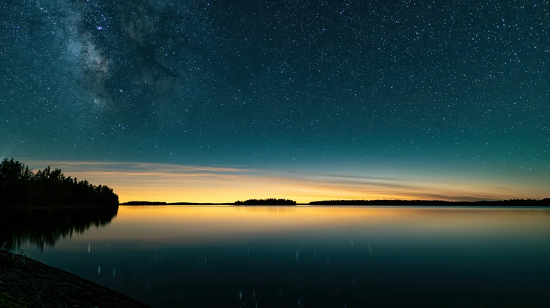 Milky way reflected in calm lake waters at twilight with forested shoreline