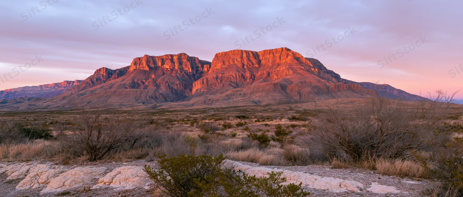 Rocky desert mountain range at sunset with sparse vegetation and colorful sky