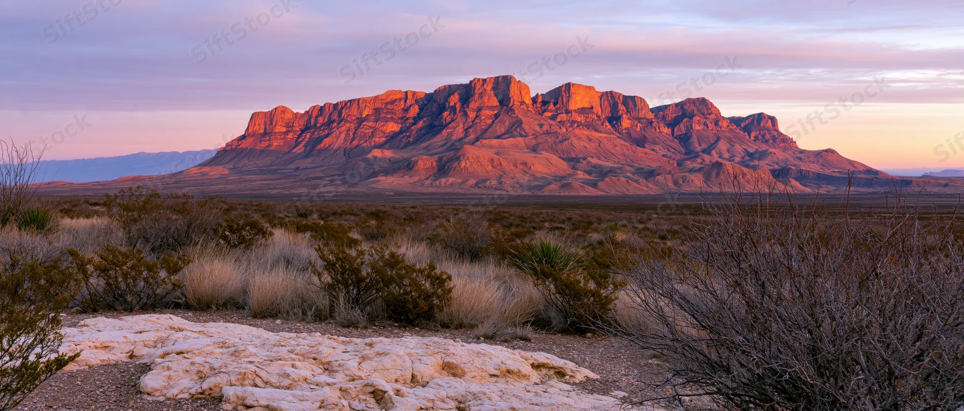 Red rock mountain formation at sunset in desert landscape with sparse vegetation and distant horizon