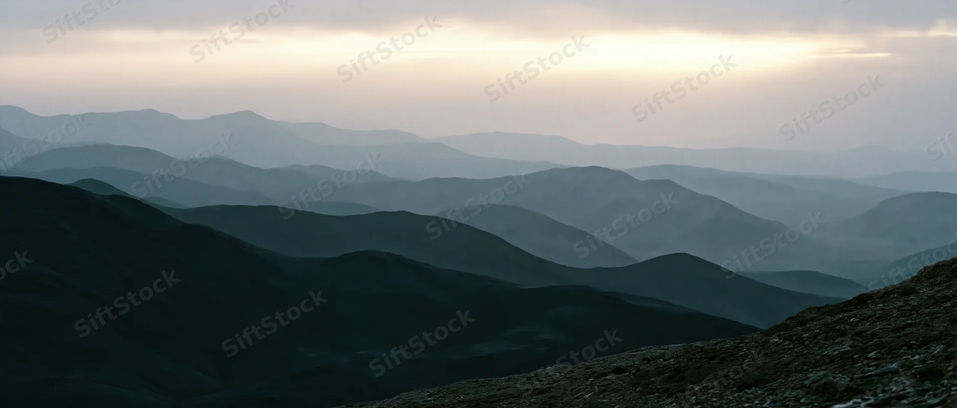 Layered mountain ridges receding into misty distance under overcast sky
