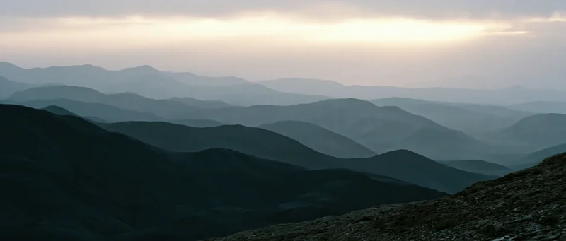 Layered mountain ridges receding into misty distance under overcast sky