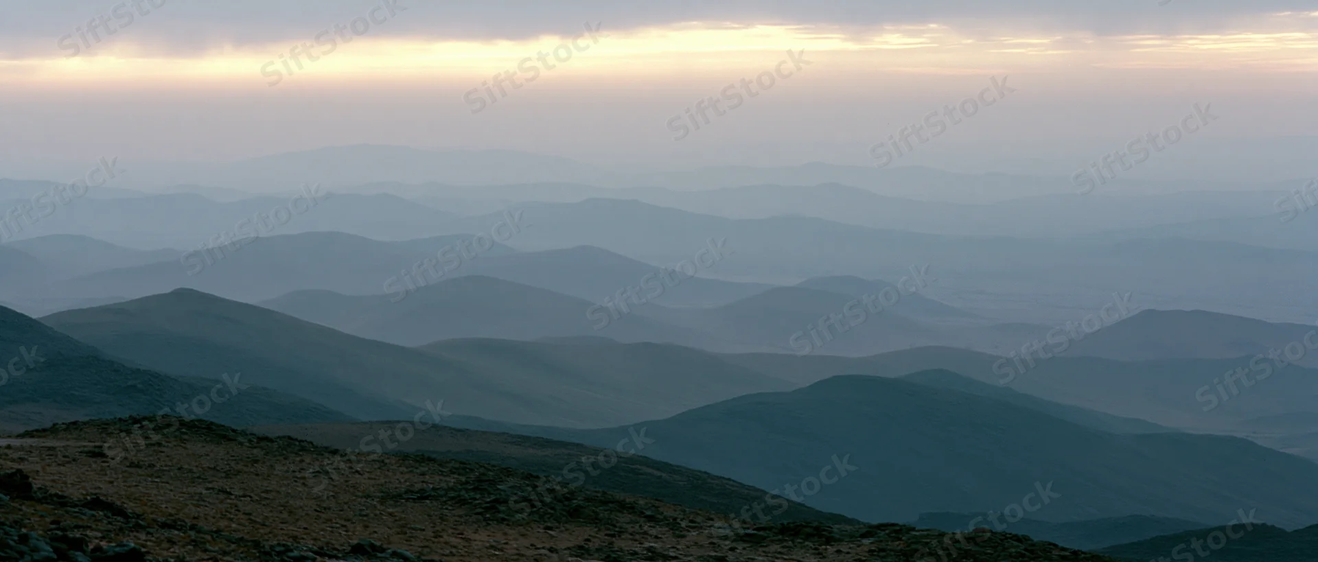 Layered mountain ranges receding into atmospheric haze under twilight sky