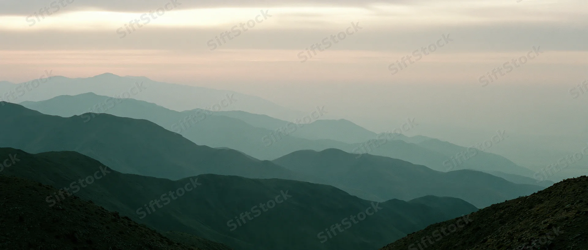 Layered mountain range silhouetted against hazy twilight sky