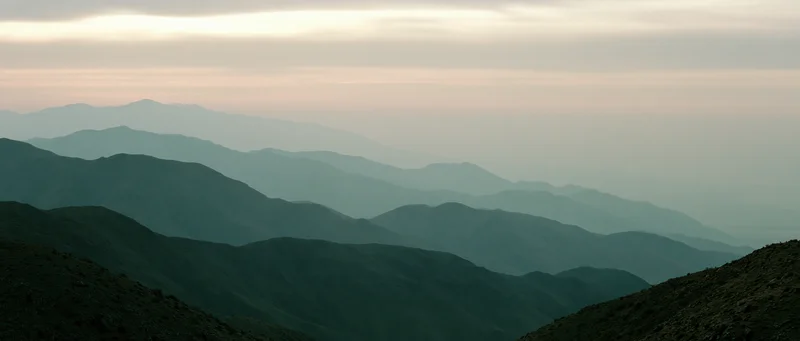 Layered mountain range silhouetted against hazy twilight sky