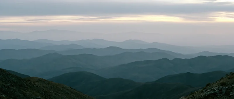 Layered mountain ranges receding into atmospheric haze under overcast sky