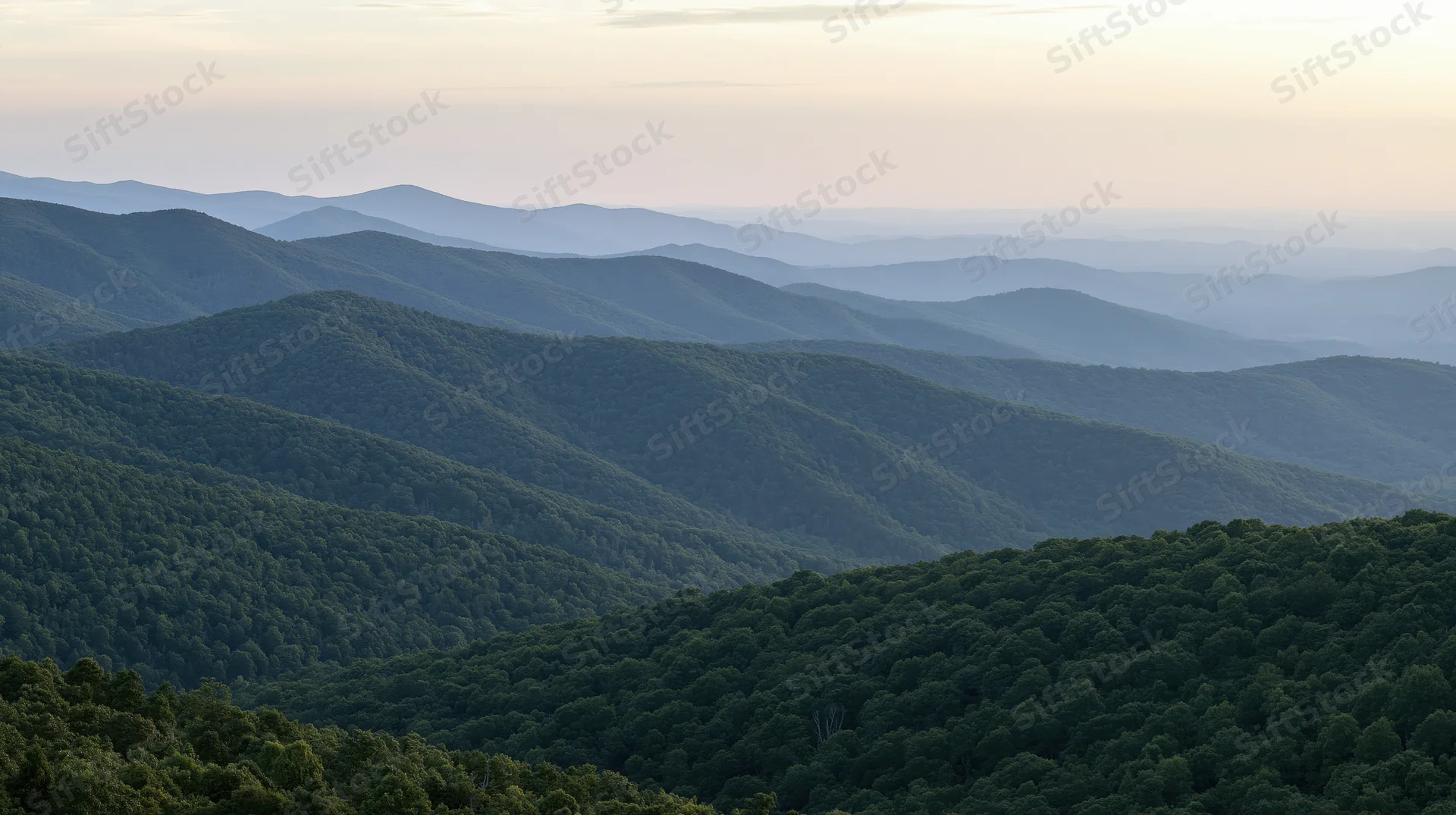Rolling forested mountains receding into hazy distance under soft twilight sky