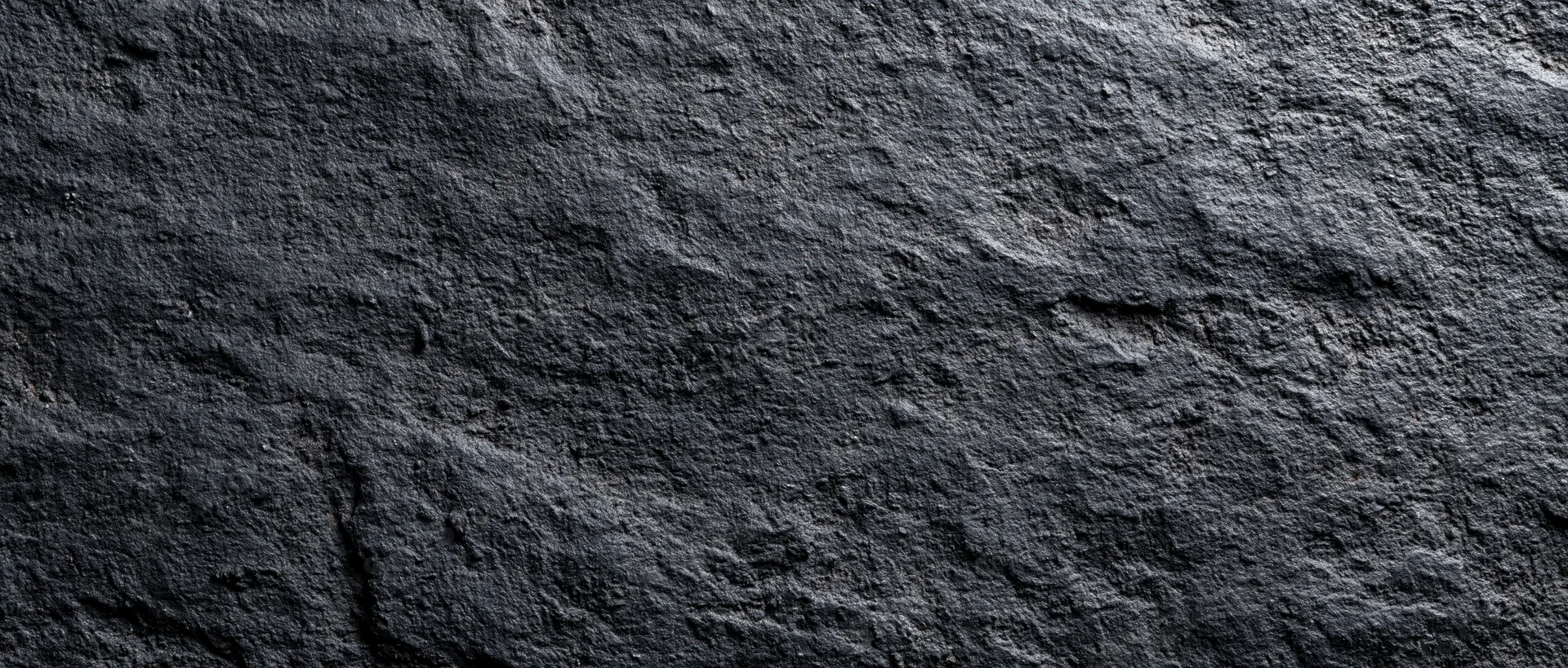 Closeup of dark rough stone surface with natural texture and uneven pattern