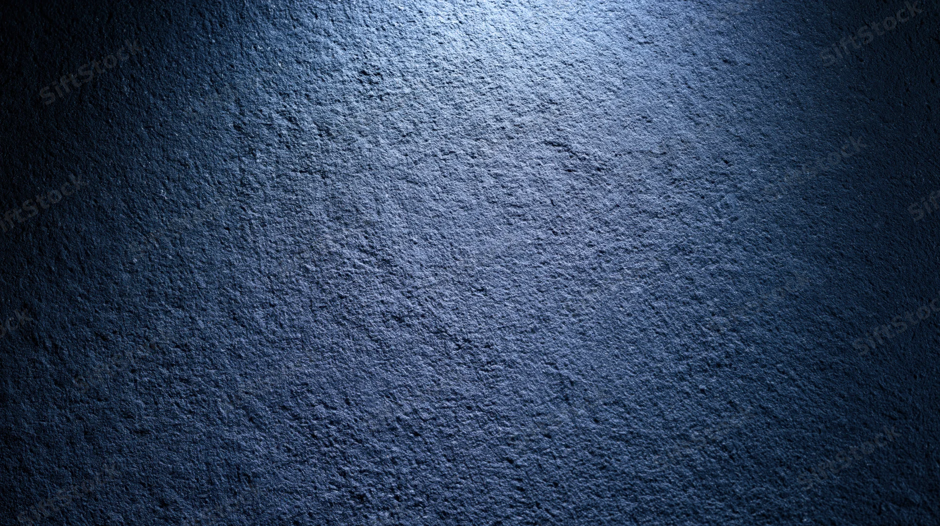 Textured blue concrete wall illuminated by a spotlight creating a gradient from light to dark