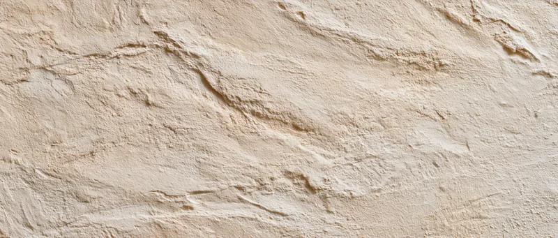 Textured plaster wall surface with uneven stucco finish in beige tone