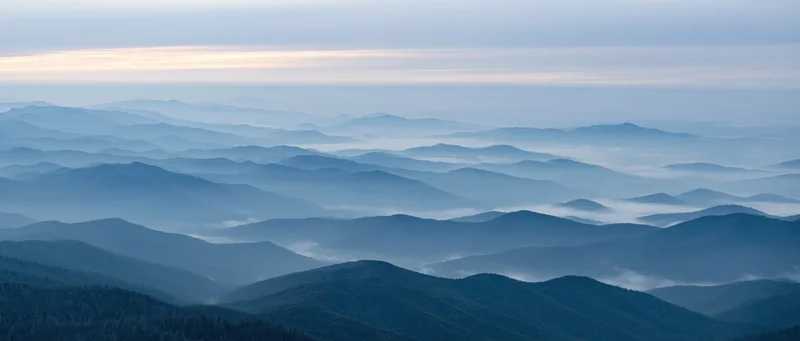 Layered mountain range with fog and forest under twilight sky