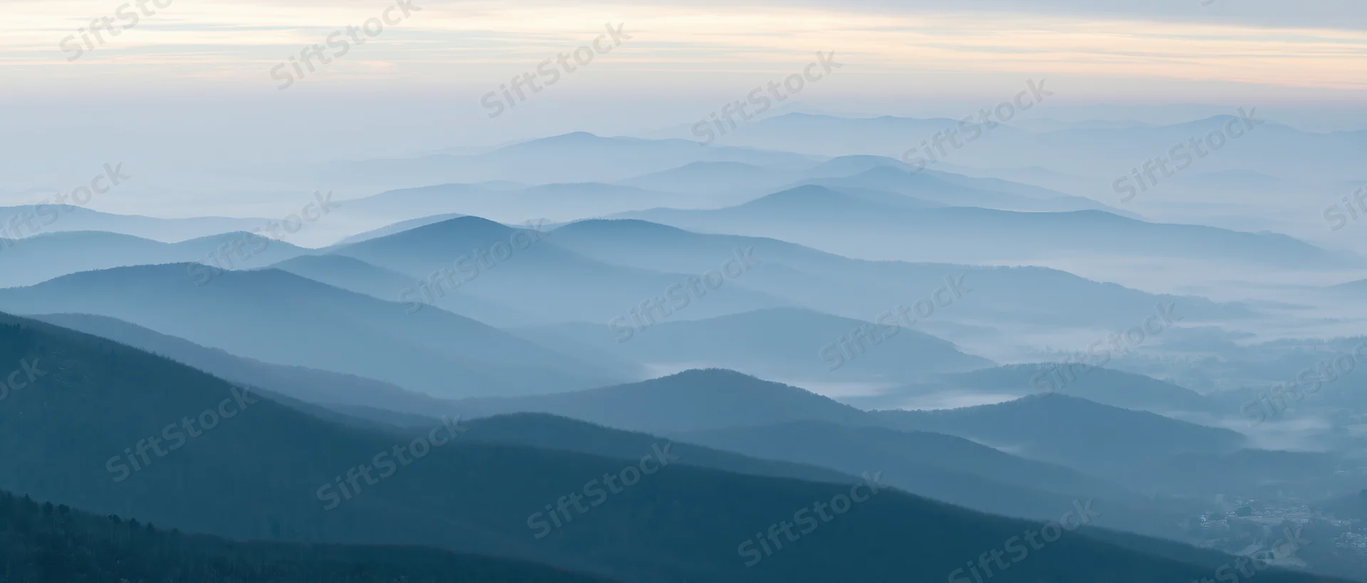 Layered mountain ridges fading into misty horizon over a forested valley at dawn
