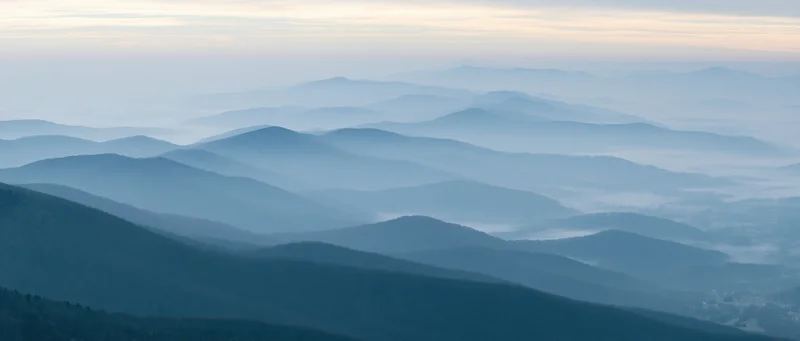 Layered mountain ridges fading into misty horizon over a forested valley at dawn