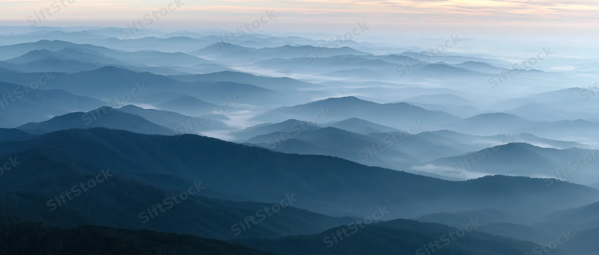 Layered mountain ridges fading into mist under soft dawn light
