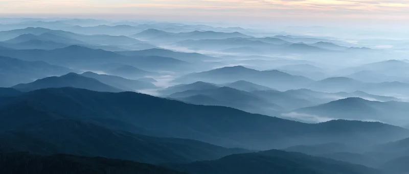 Layered mountain ridges fading into mist under soft dawn light