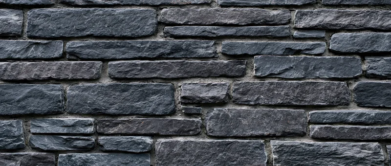 Dark gray stone wall with horizontal stacked masonry and mortar joints, exterior surface texture