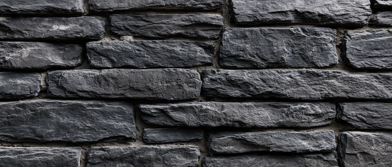 Dark gray stone wall with horizontal stacked slate blocks and mortar joints, exterior architectural surface