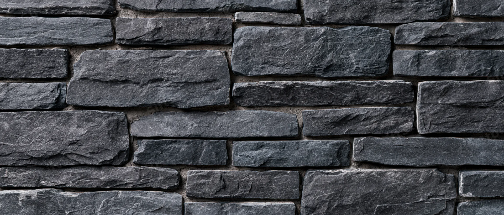 Gray slate stone wall with rough texture arranged in staggered pattern for exterior building facade