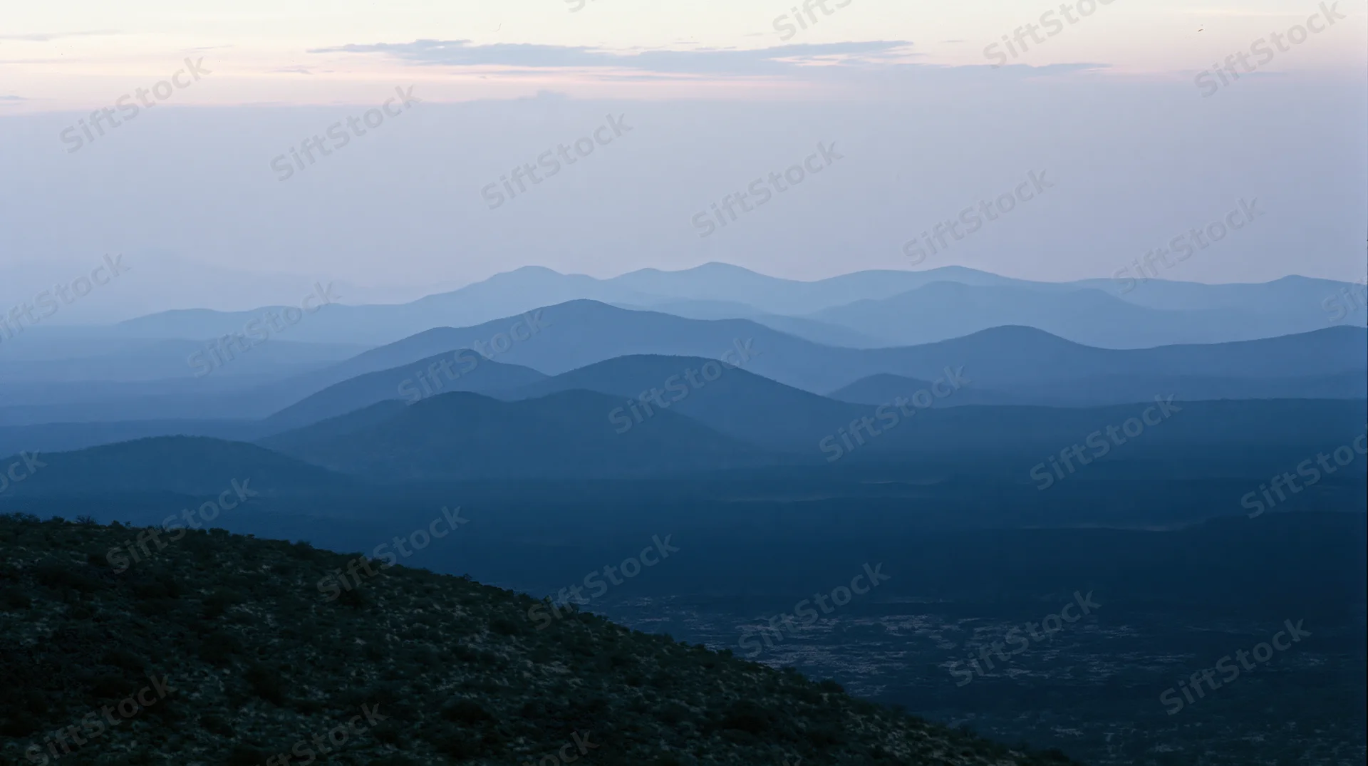 Layered mountain ridges receding into the distance under a hazy twilight sky