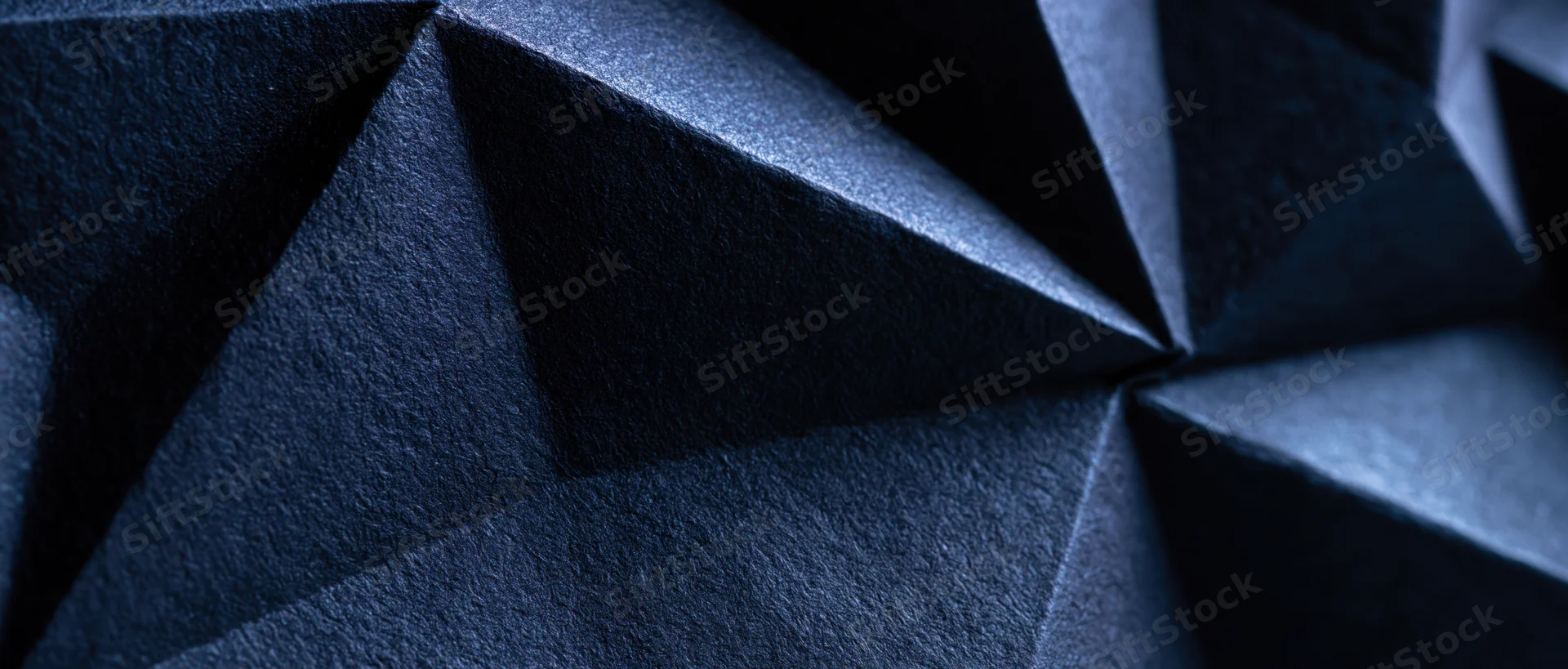 Dark blue faceted geometric surface with sharp angles and shadows