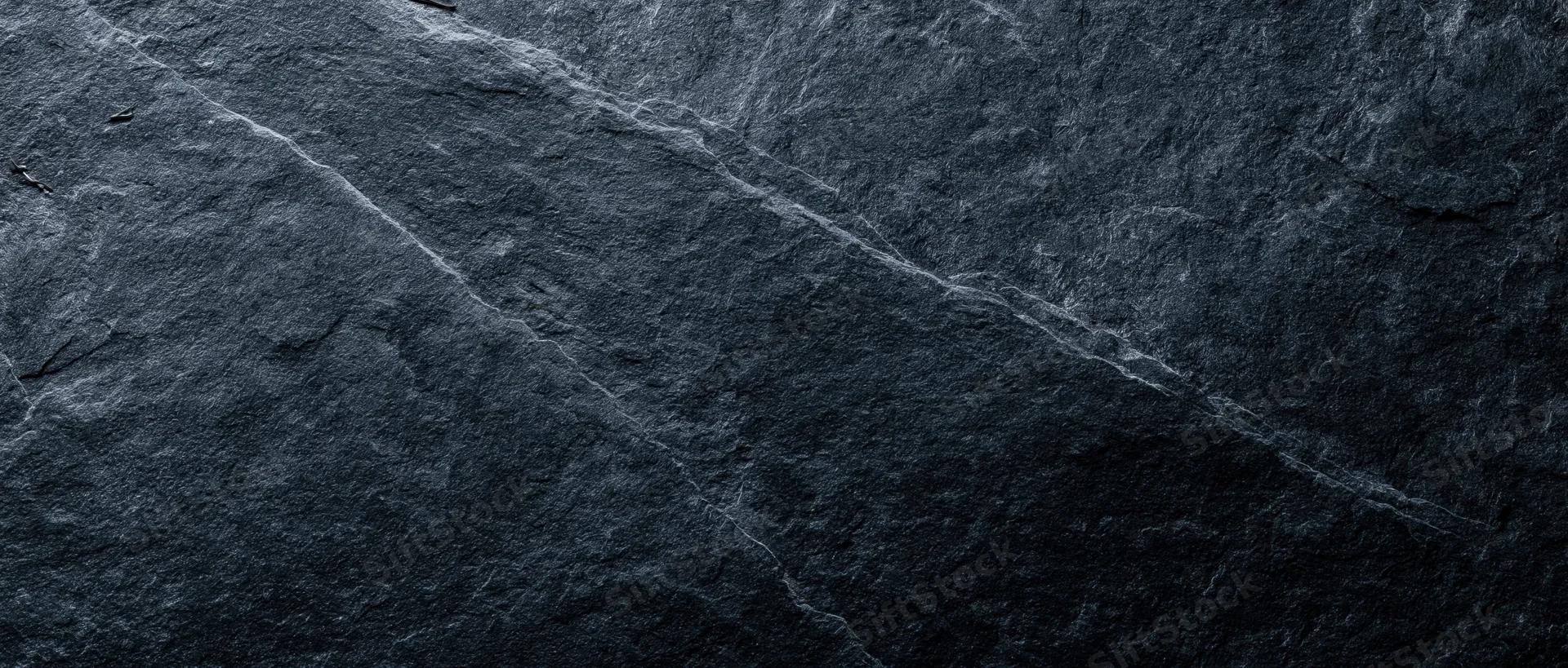 Dark slate stone surface with natural veins and cracks, used as a textured background