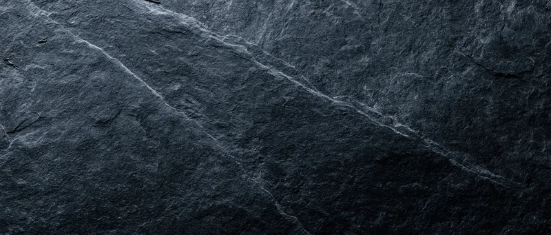 Dark slate stone surface with natural veins and cracks, used as a textured background