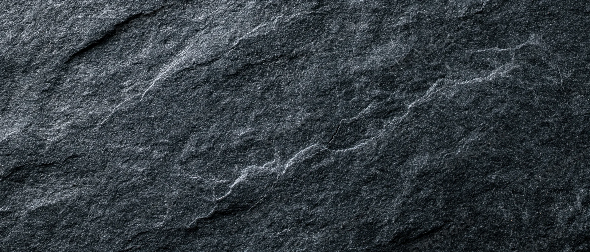 Closeup of dark slate stone surface with natural cracks and texture