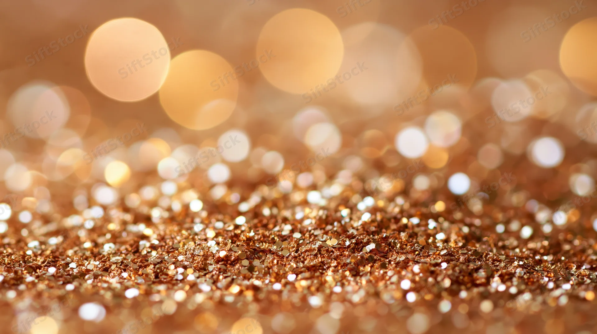 Golden glitter scattered across a surface with blurred bokeh lights in the background