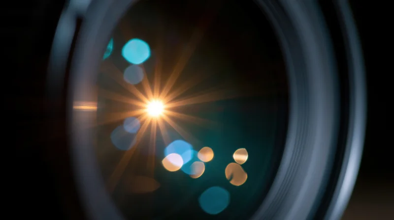 Camera lens with starburst light flare and colorful bokeh reflections in the glass