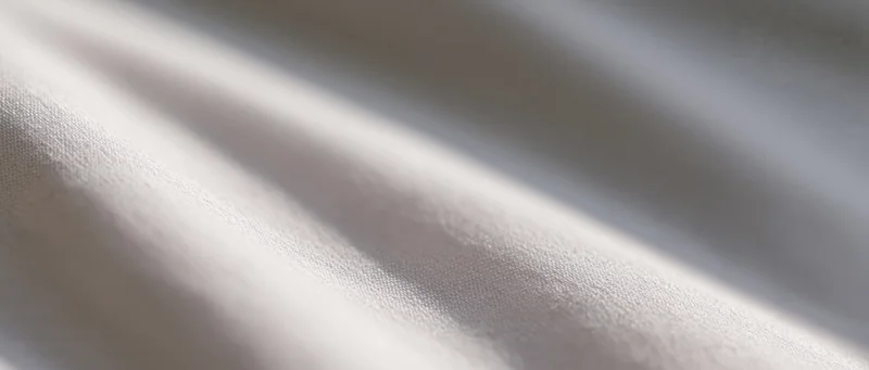 Closeup of white fabric with soft folds and natural light creating subtle shadows and texture