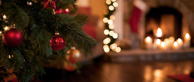 Christmas tree with red and gold ornaments near a lit fireplace in a cozy living room interior