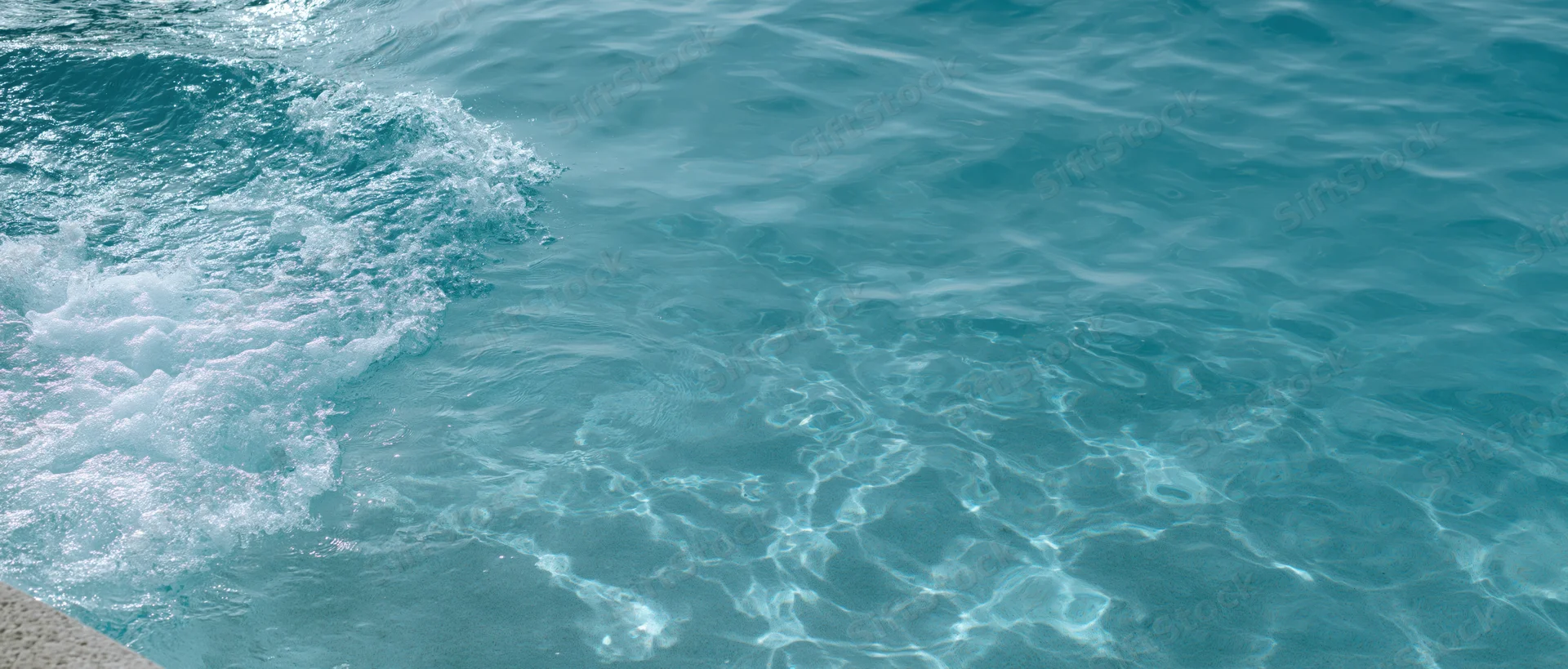 Turquoise ocean water with small waves breaking near a stone edge