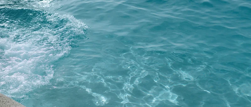 Turquoise ocean water with small waves breaking near a stone edge