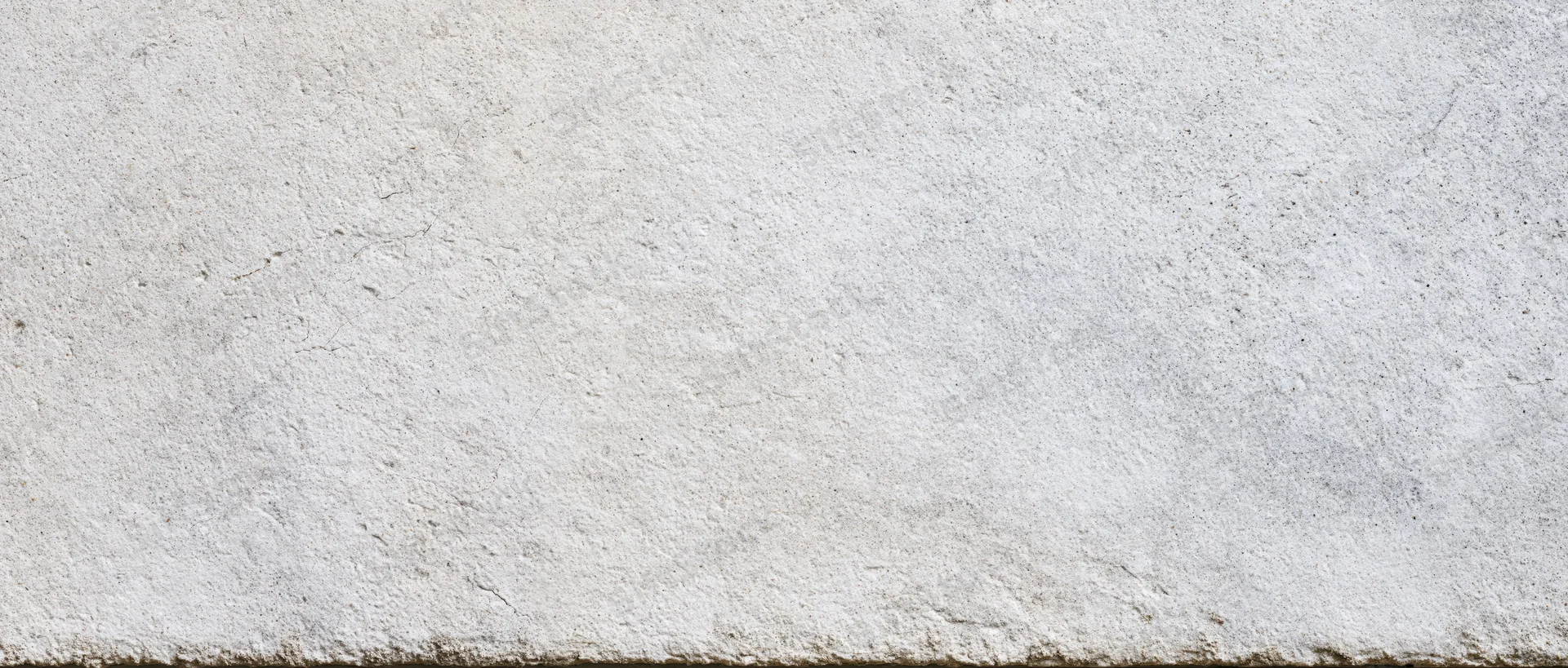 Close-up of a textured concrete wall surface with visible grain and minor imperfections, showing a horizontal edge at the bottom