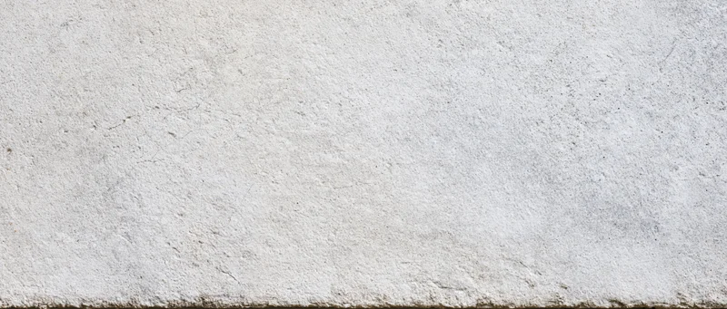 Close-up of a textured concrete wall surface with visible grain and minor imperfections, showing a horizontal edge at the bottom