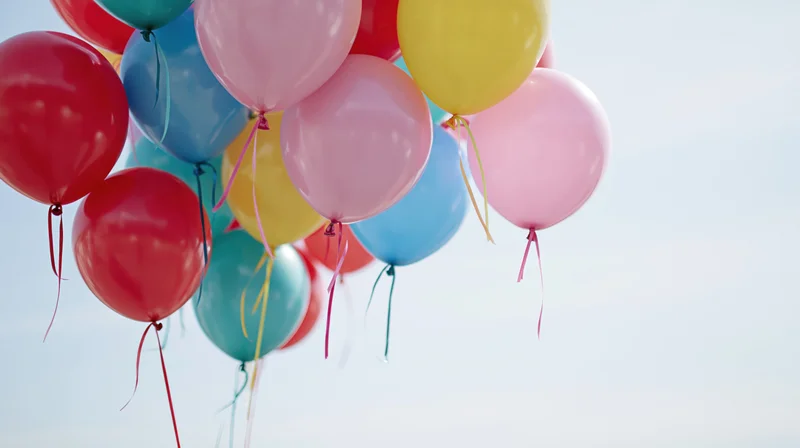 Cluster of colorful balloons floating in the sky against a clear background