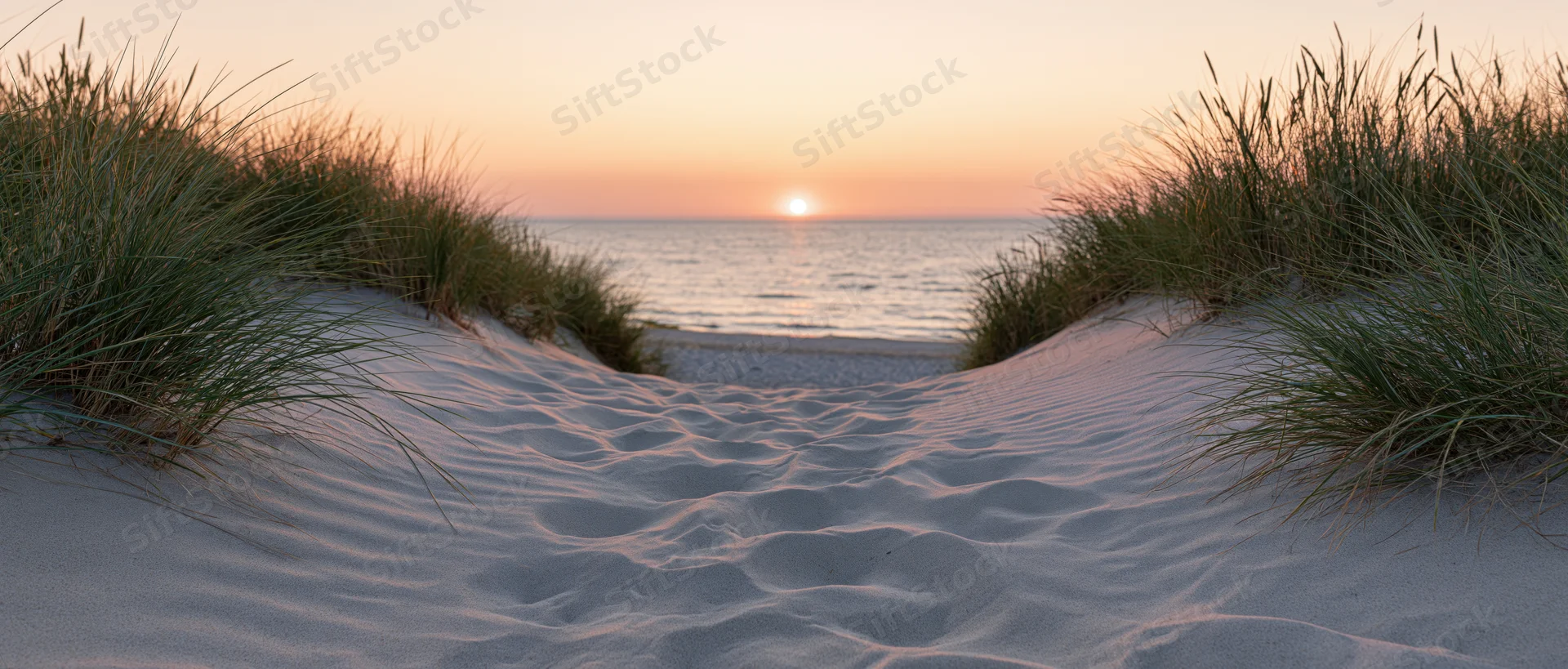 Sandy path between dunes leading to ocean at sunset