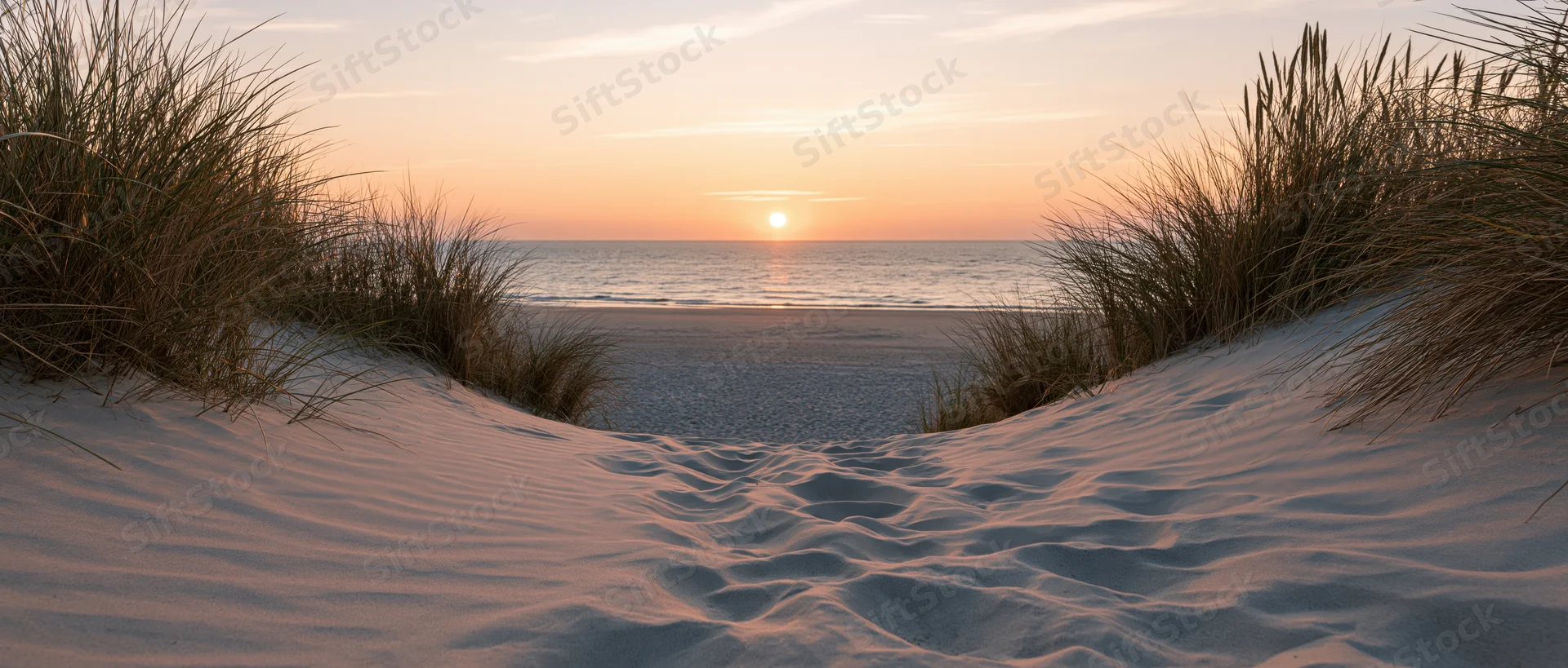 Sandy path between dunes leading to ocean at sunset